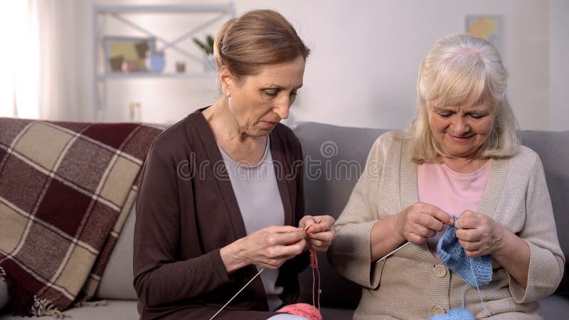 Two senior women knitting sitting nursing home sofa, retirement hobby, relax