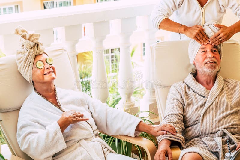 Two seniors and pensioeners in a beauty traetment together - women doing a massage in the face of the mature men - women with zucchini on her eyes. Two seniors and pensioeners in a beauty traetment together - women doing a massage in the face of the mature men - women with zucchini on her eyes