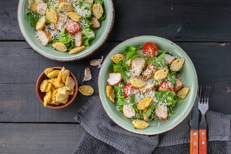 Two servings of Caesar salad with fried chicken, parmesan and croutons on a dark rustic background. To pview stock photo Two servings of Caesar salad with fried chicken, parmesan and croutons on a dark rustic background. To pview stock photo