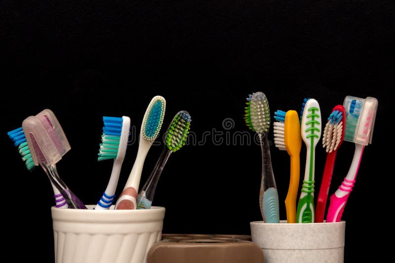 Two Sets of Toothbrushes in Plastic Cups on Black Background To