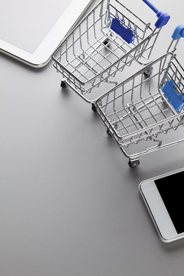 Two shopping carts, modern mobile phone and tablet on a gray background. Two shopping carts, modern mobile phone and tablet on a gray table background stock photography Two shopping carts, modern mobile phone and tablet on a gray background. Two shopping carts, modern mobile phone and tablet on a gray table background stock photography