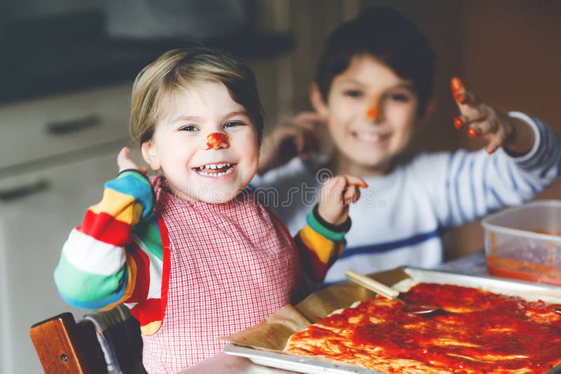 Two siblings, little children making italian pizza at home. Cute toddler girl and school boy having fun in home kitchen. Indoors. Brother and sister, family royalty free stock photos