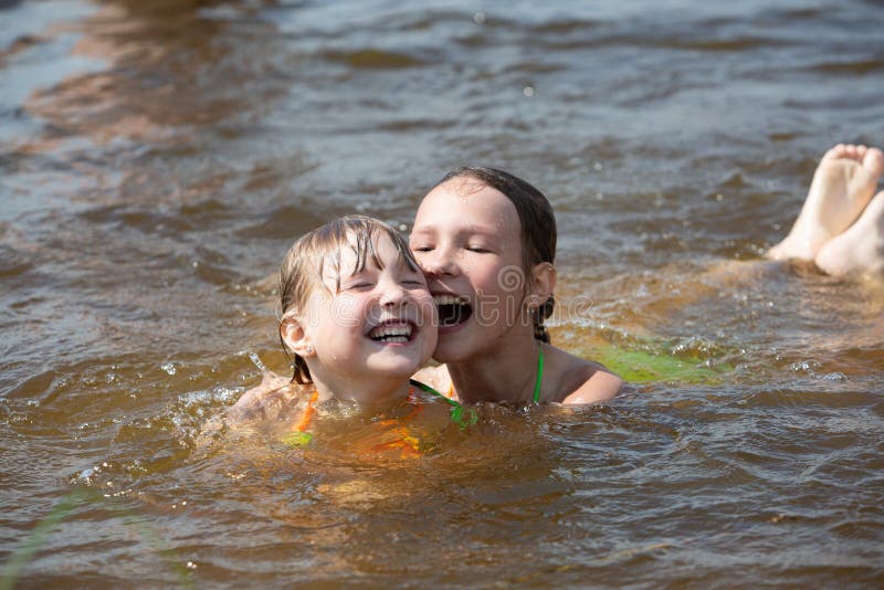 Two Sisters Have Fun Playing Swimming In A Warm River In The Summer
