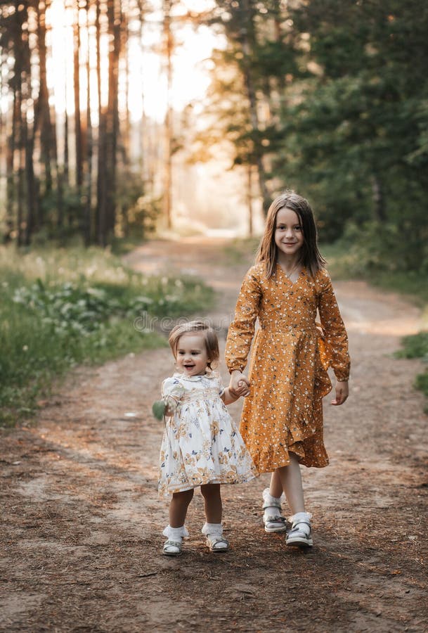Two Sisters Run through the Forest Holding Hands. Summer Sunny Day and