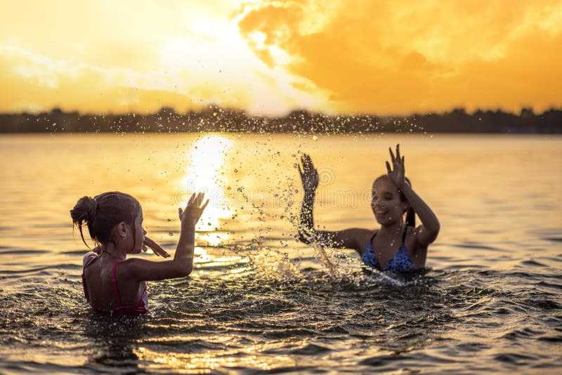 Two Sisters Splashing Water Playing In The Lake At Sunset Background