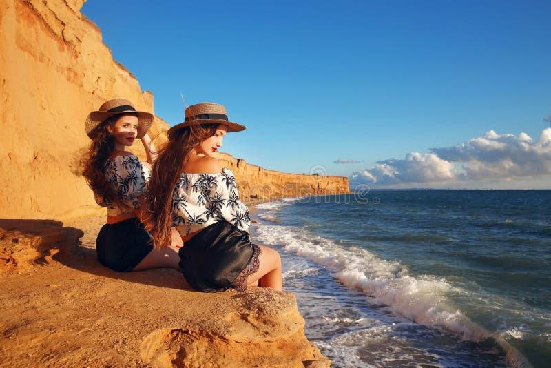 Two slim twins girl in straw hat relax on the beach enjoying life, summer sunset outdoor portrait. People Girlfriend freedom style