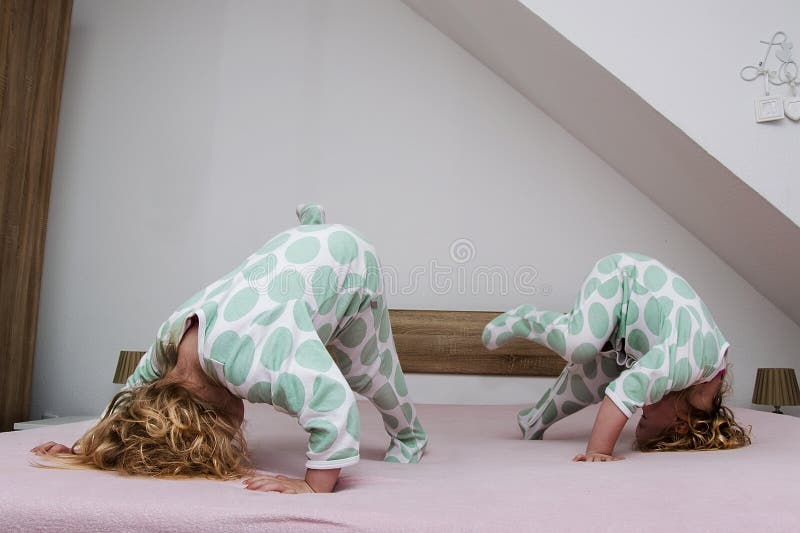 Two small identical twin sisters in identical pajamas, actively having fun on the parent& x27;s bed