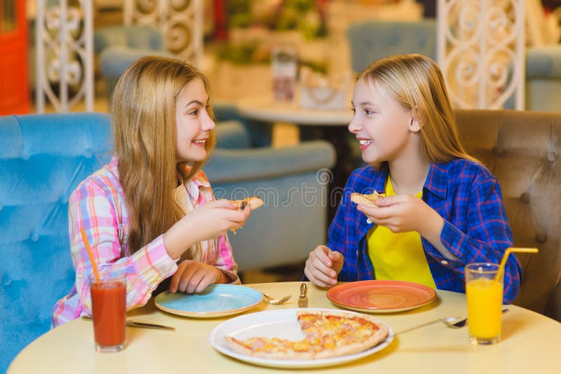 Two Smiling Girls Eating Pizza and Drinking Juice Indoor Stock Photo