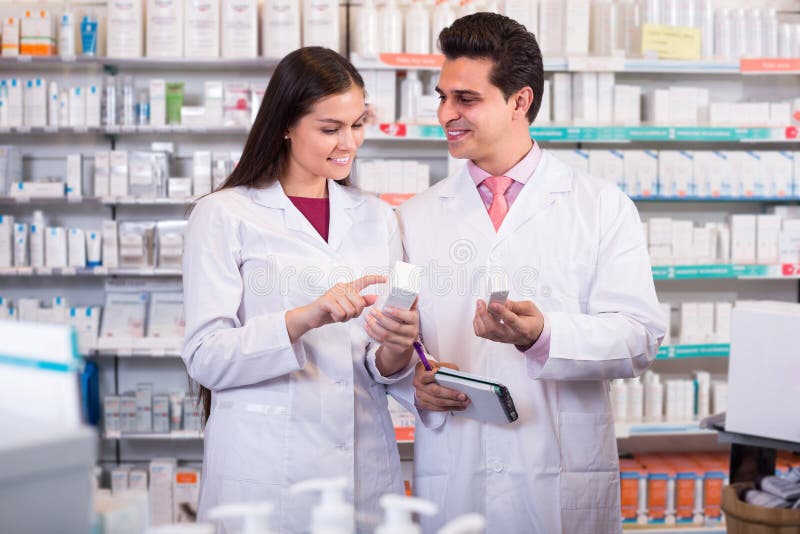 Two smiling pharmacists in uniform at the work in modern pharmacy. Two smiling pharmacists in uniform at the work in modern pharmacy.