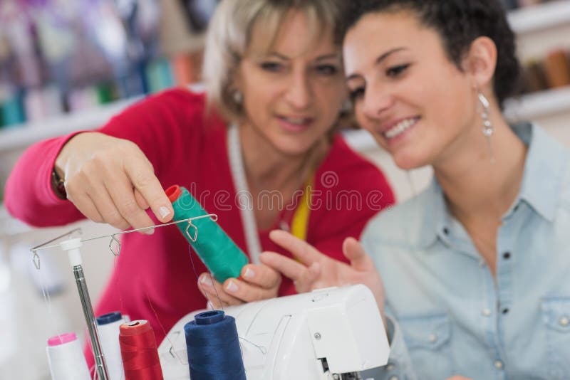 Two Smiling Women Using Sewing Machine while Holding Bright Fabric