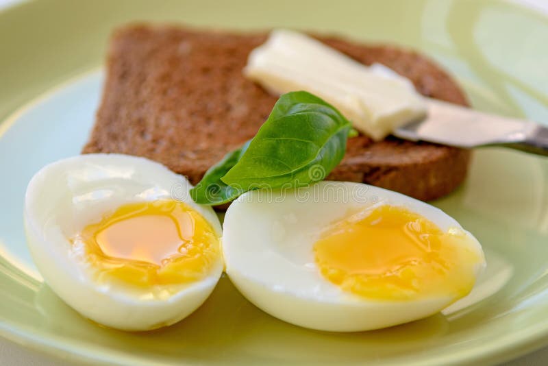 Two Softboiled Egg Halves on a Plate. Basil Leaf, Toast and Butter