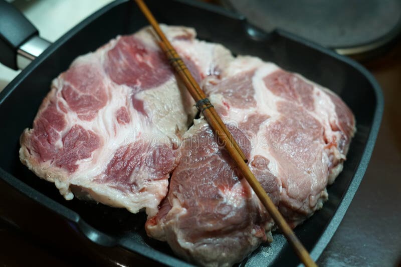 Two Still Raw Large Pork Steaks are Fried in a Frying Pan at Home