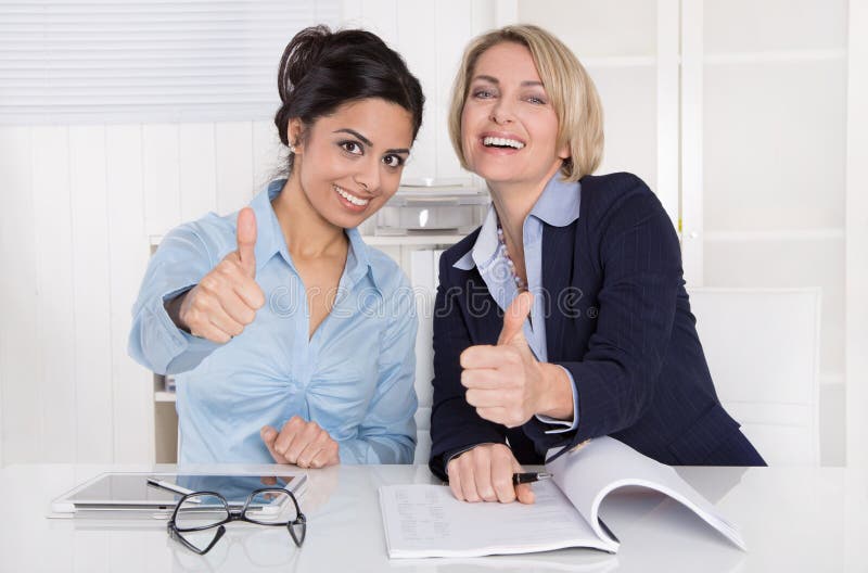 Two successful business women with thumbs up at office. stock photos