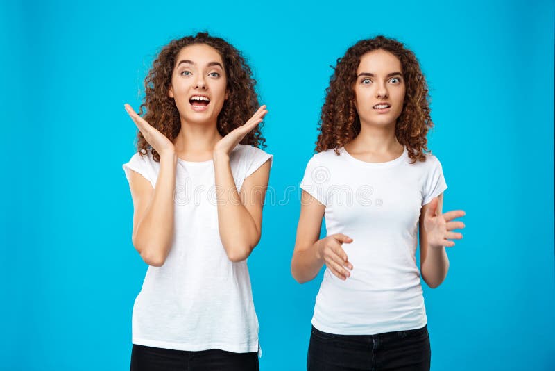 Two Surprised Girls Twins Pointing Finger Away Over Blue Background 