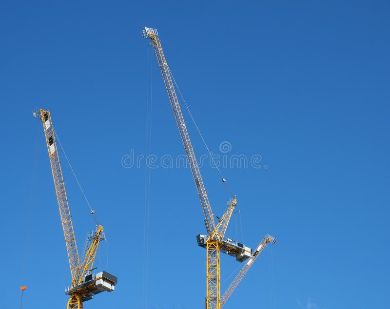 Two tall yellow construction cranes working against a blue sky stock photography Two tall yellow construction cranes working against a blue sky stock photography