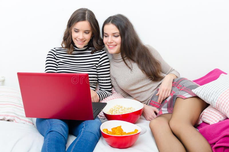 Two teenage girls using notebook and eating snacks while sitting