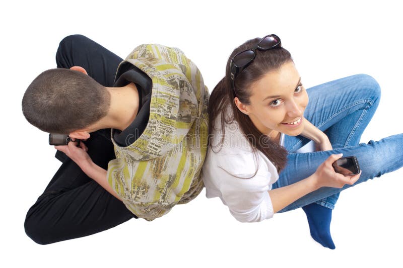 Two teenagers sitting on white with cellphones