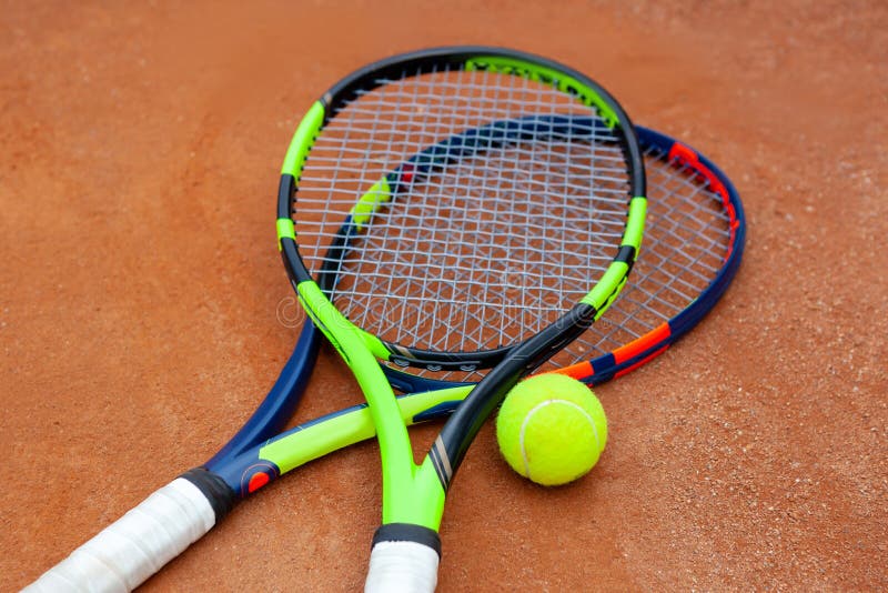 Two tennis rackets and yellow tennis ball lie on the clay court