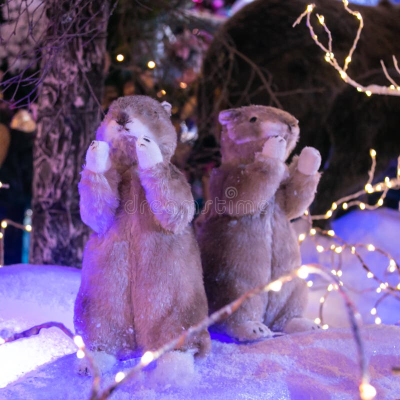 Two toy gophers with raised paws against the background of an artificial forest and snow. Christmas and New Year concept.