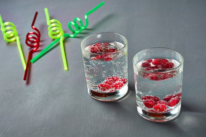 Two transparent glasses full of drinks with red berries near spiral straws lies on scratched dark cement stock images Two transparent glasses full of drinks with red berries near spiral straws lies on scratched dark cement stock images