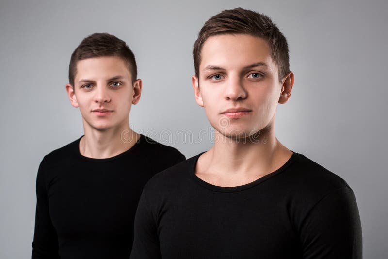 The two twin brother stand on the gray background stock photo.