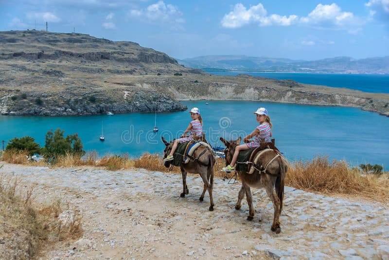Two twin girls riding donkeys on a mountain road to the sea. Rhodes. Greece stock photo Two twin girls riding donkeys on a mountain road to the sea. Rhodes. Greece stock photo