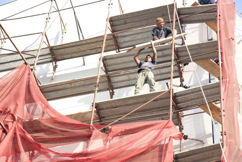 Two unprotected construction workers on the scaffold during building facade reconstruction, an unsafe, hazard  and dangerous