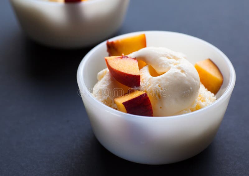 Two vanilla ice-cream with peach on dark background, selective focus. Two vanilla ice-cream with peach on dark background, selective focus