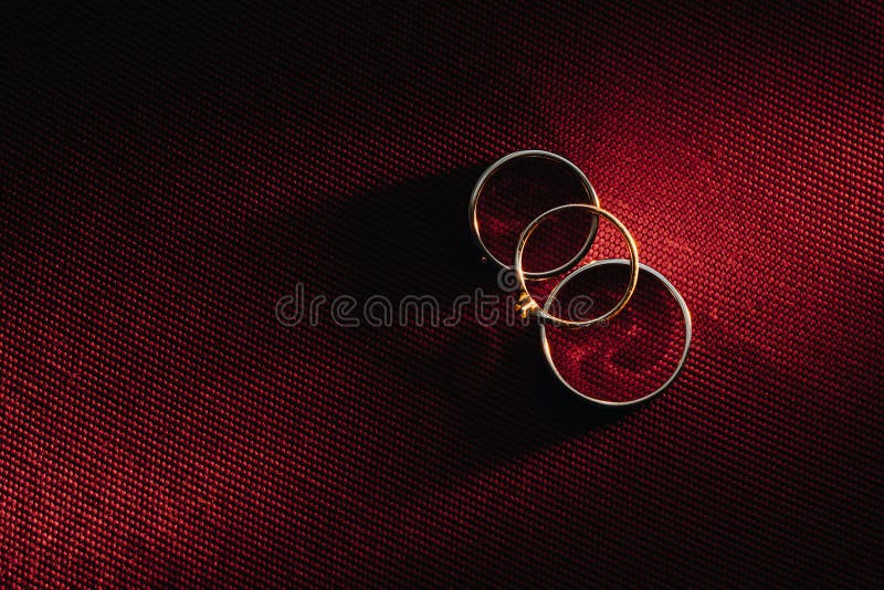 Two wedding rings and one engagement ring on a red background. three Gold rings of a couple in love.Concept of love.Wedding ring