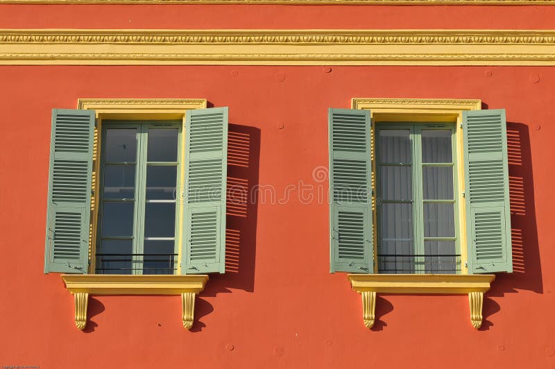 Two windows with window shades open on a red wall