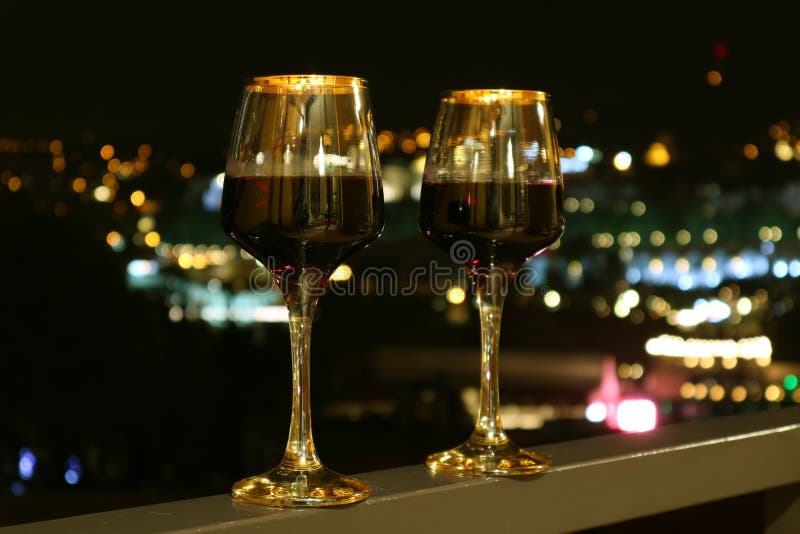 Two Wine Glasses On The Balcony With Blurry City Night View In The Background