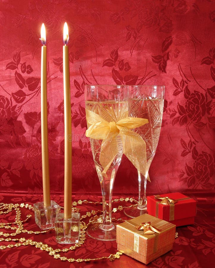 Two wine glasses with champagne, gifts and golden candles on red