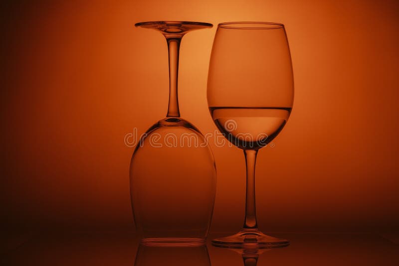 Two wine glasses on orange background. One glass upside down