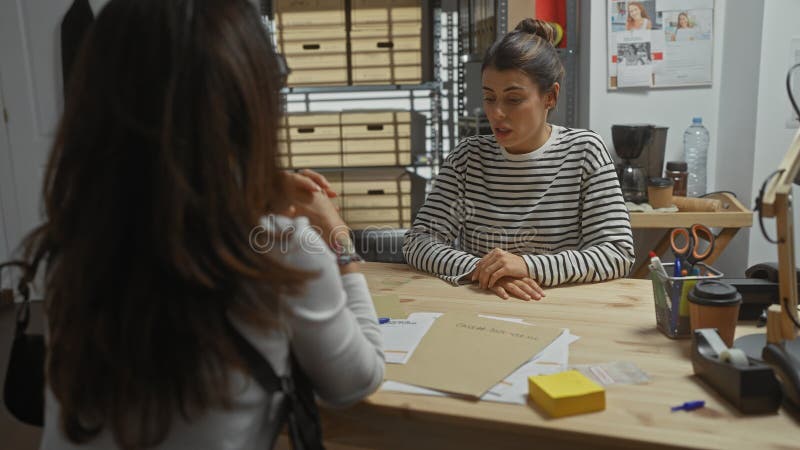 Two women converse intently in an office with paperwork suggesting law enforcement or detective work. Detective paperwork stock images, royalty-free photos and pictures