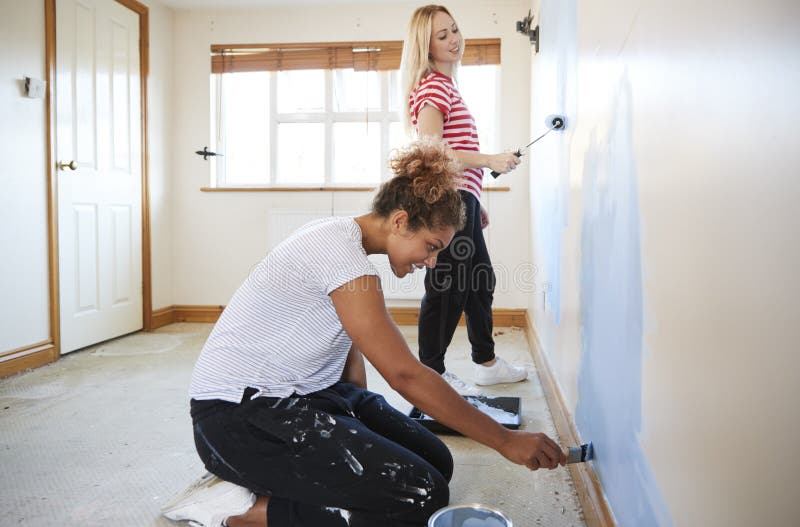 Two Women Decorating Room In New Home Painting Wall