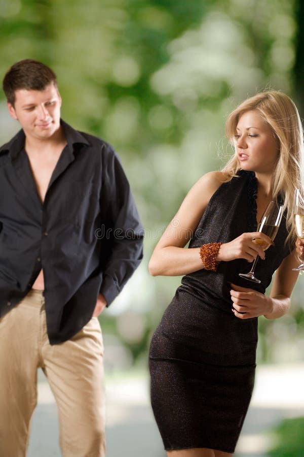 Two women holding glasses with champagne, young man looking at them and smiling, outdoors, focus on blond woman. Two women holding glasses with champagne, young man looking at them and smiling, outdoors, focus on blond woman