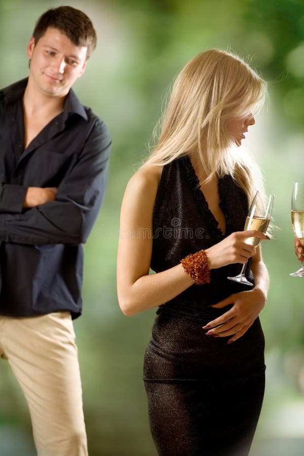 Two women holding glasses with champagne, young man looking at them, outdoors, focus on blond woman. Two women holding glasses with champagne, young man looking at them, outdoors, focus on blond woman