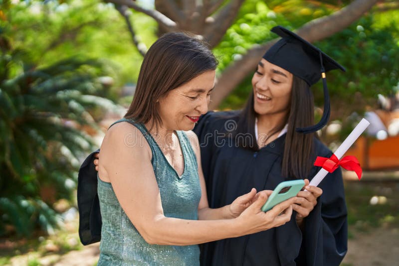 Two women mother and graduated daughter using smartphone at park stock image