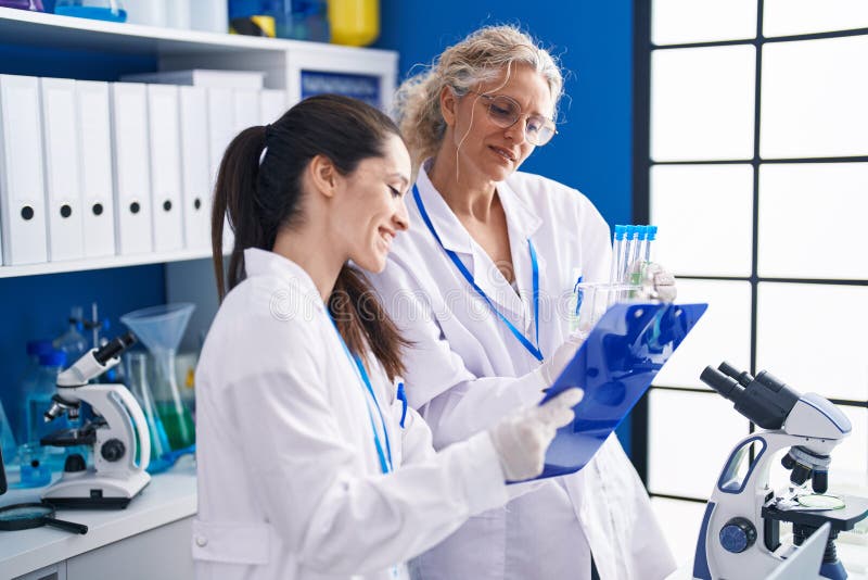 Two Women Scientists Writing on Document Holding Test Tubes at
