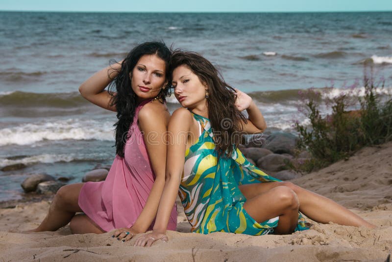 Two women seating on sand near the sea