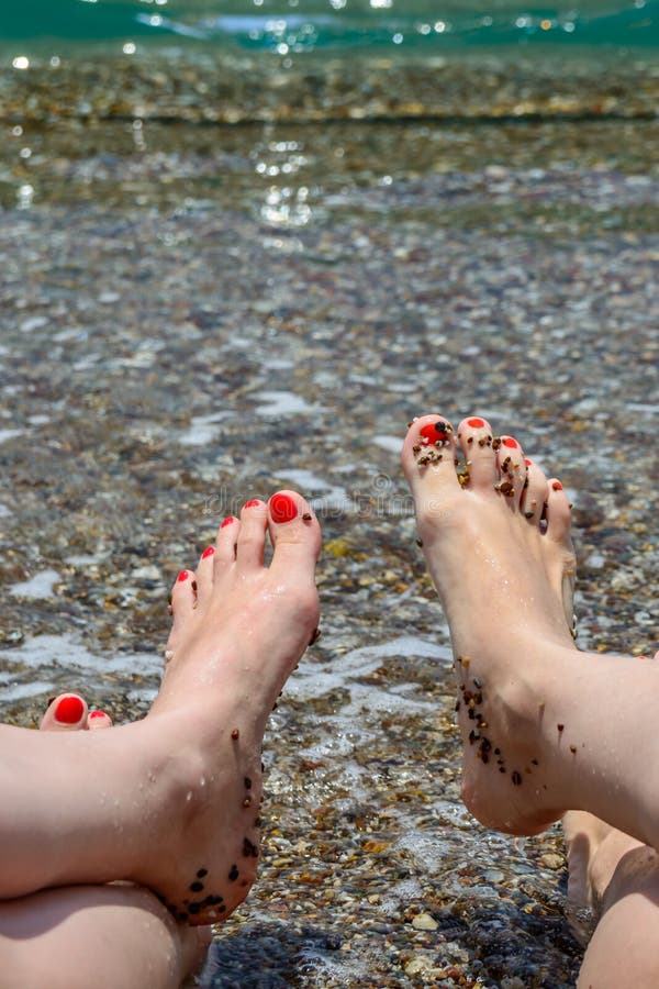 Two women showing their feet with red painted nails over the ocean background