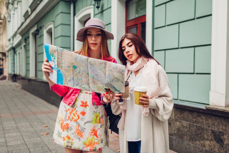 Two women tourists searching for right way using map in Odessa. Happy friends travelers showing direction and laughing