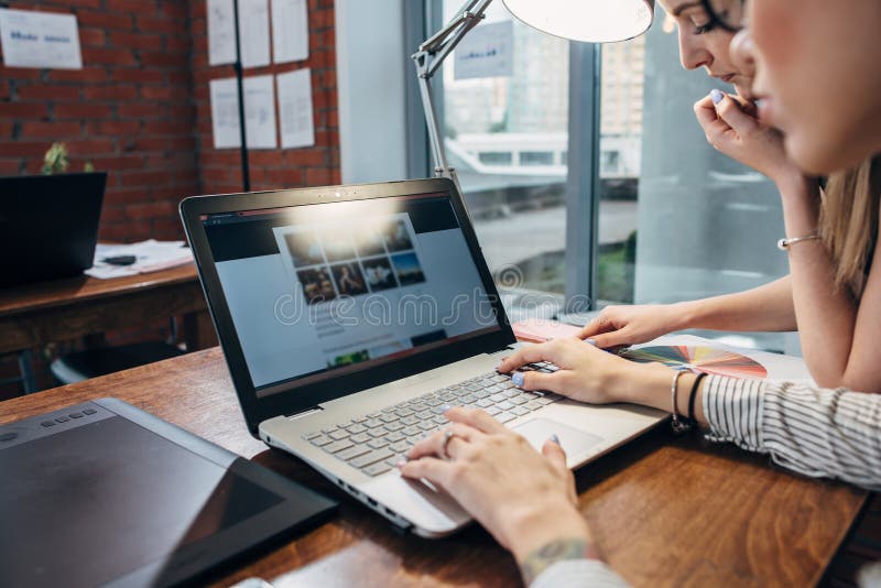 Two women working on new website design choosing pictures using the laptop surfing the internet royalty free stock images