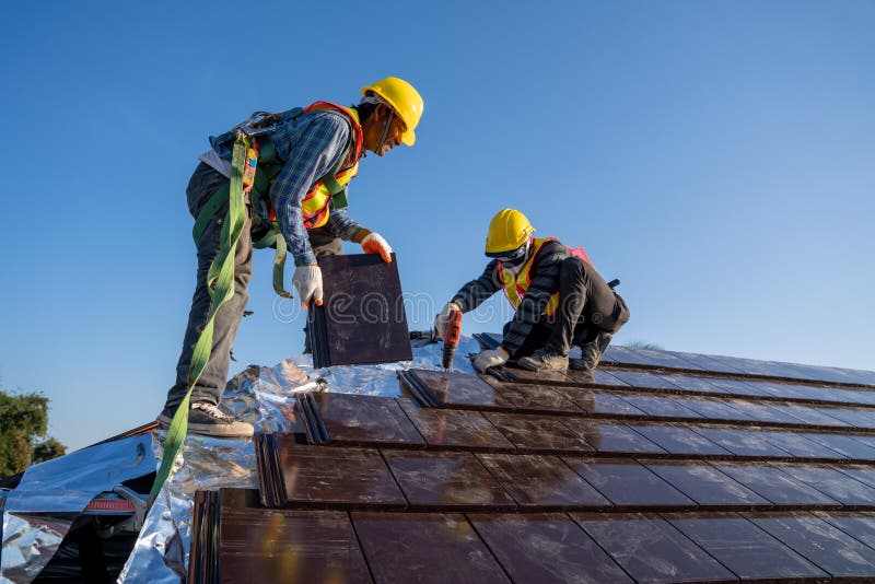 Roofing contractors with fall protection, roof safety harness, ropes are  finishing to install asphalt roof shingles on the gable house roof. Roofing  construction. Stock Photo
