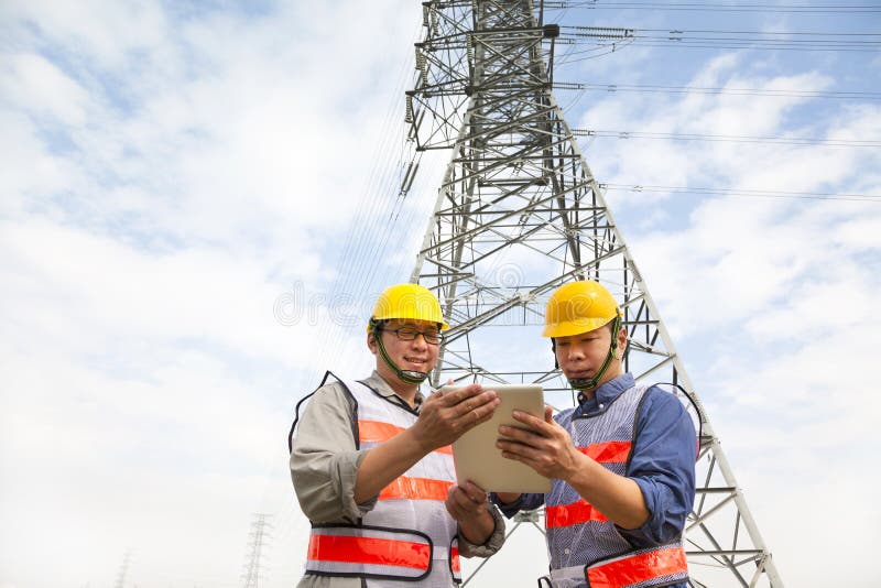 Two workers standing before electrical power tower royalty free stock images