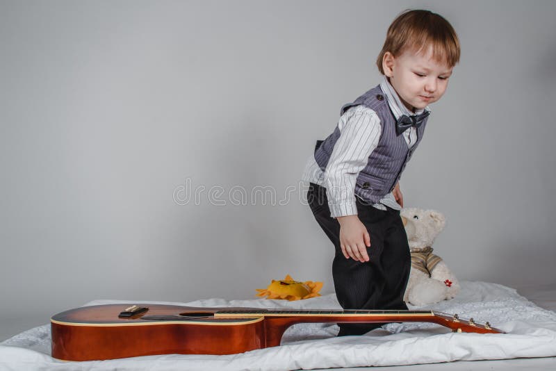 Two year old Caucasian boy in bow tie and vest with acoustic guitar on grey background stock photography Two year old Caucasian boy in bow tie and vest with acoustic guitar on grey background stock photography
