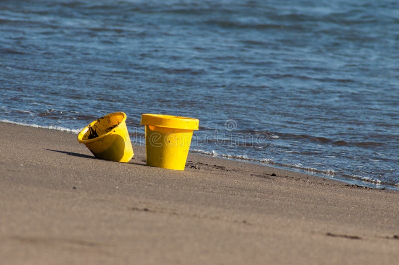 Yellow Toy Buckets Filled with Sand Left on the Beach Stock Image