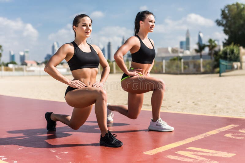 Strength in teamwork. Two young attractive women athletes exercise on the beach doing squats with a sunrise and ocean in the stock photography Strength in teamwork. Two young attractive women athletes exercise on the beach doing squats with a sunrise and ocean in the stock photography