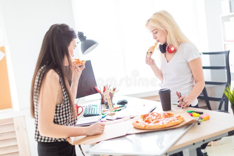 Two girls eating pizza in the office.