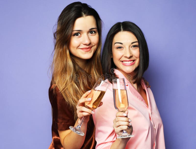 Two young beautiful women dressed in pajamas drink champagne and have fun